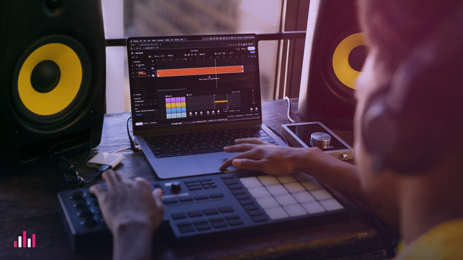 Producer working on a laptop DAW with a pad controller between studio monitors