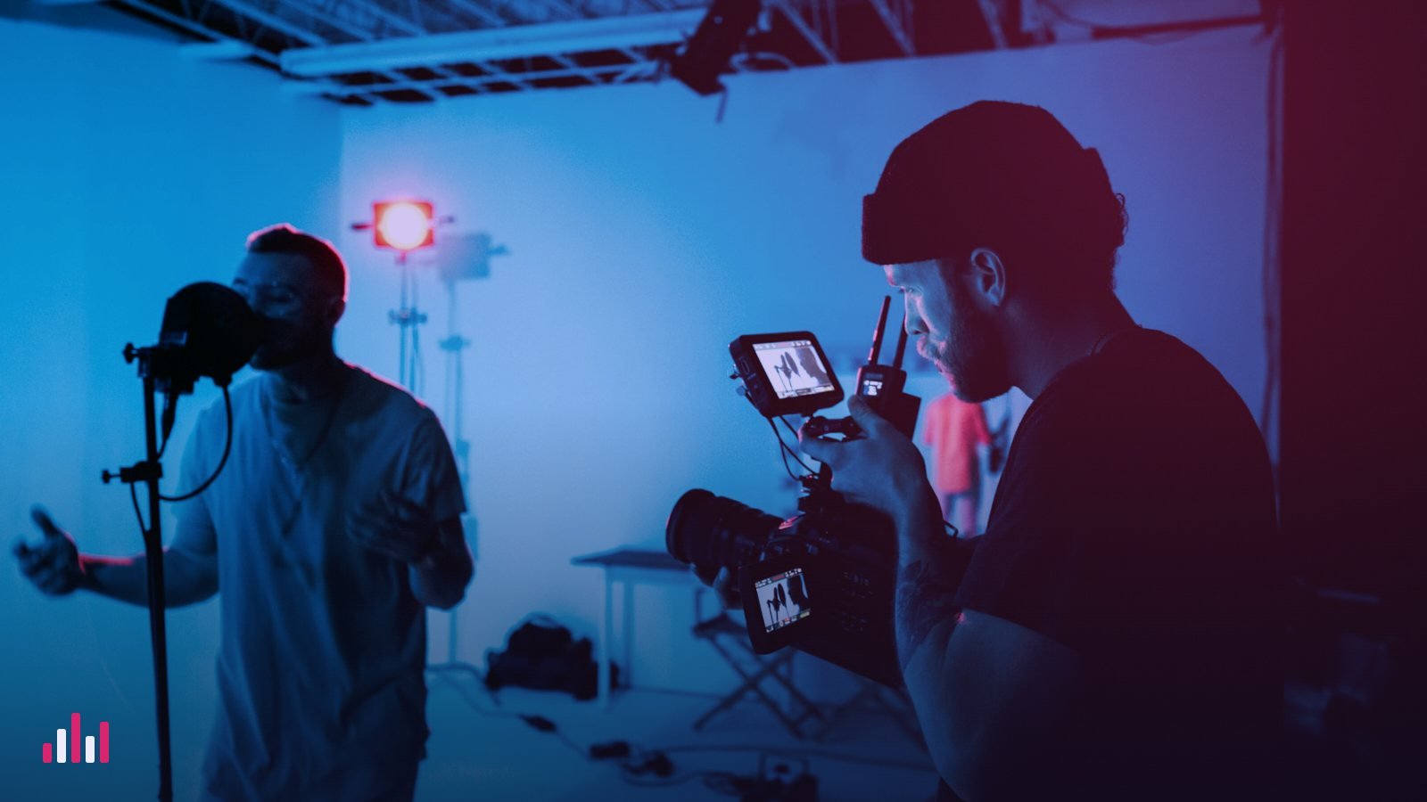 Singer performing at a microphone while a videographer films in a blue-lit studio